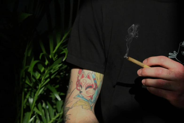 person in black shirt smoking a cigarette next to plant