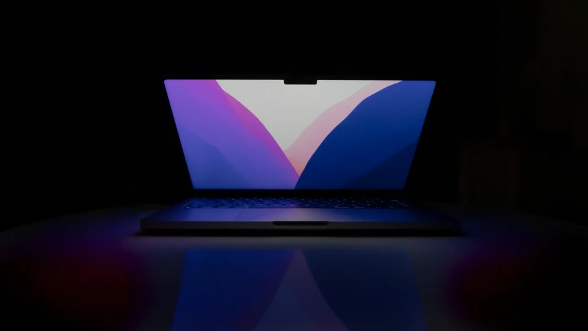 a blue laptop on a black table with light shining on it