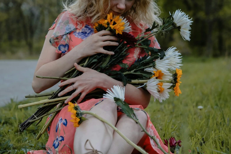 a woman holding flowers in her hands while sitting on the grass