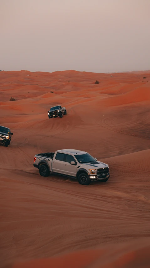 four trucks in the desert driving on sand dunes