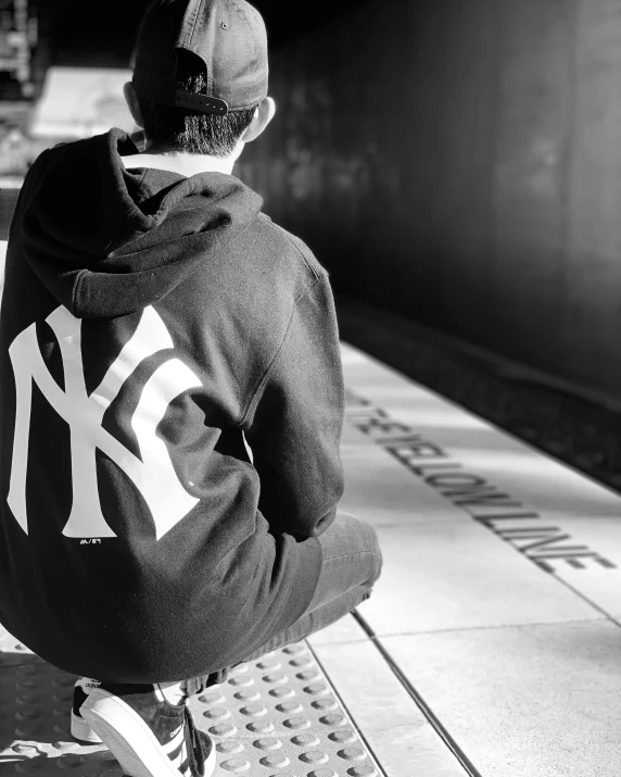 man sitting on train platform in baseball cap and sweater