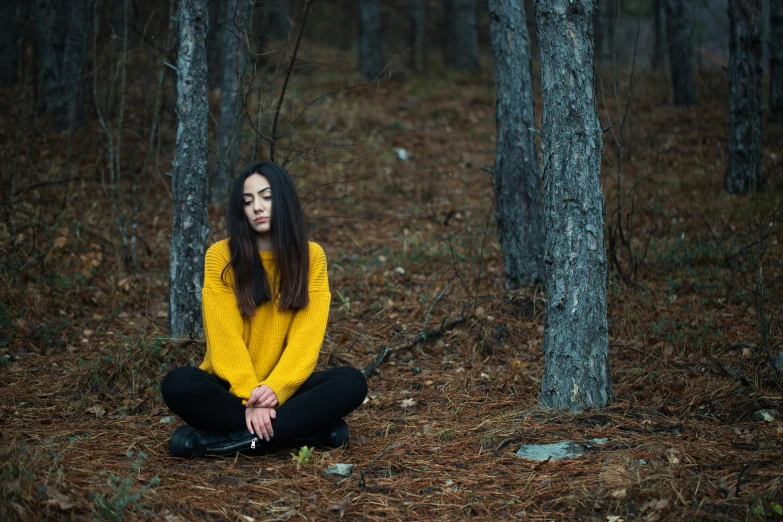 a woman sits in the woods with her legs crossed