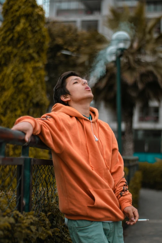 a person in an orange hoodie leaning against a fence