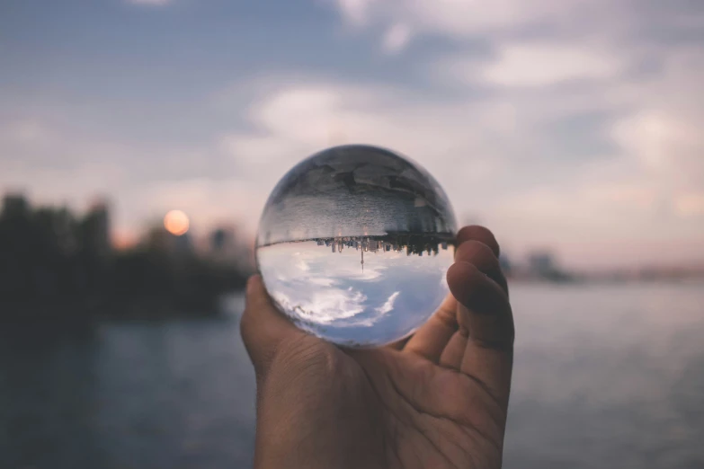 a hand holding a crystal ball with a sunset and a lake in the background