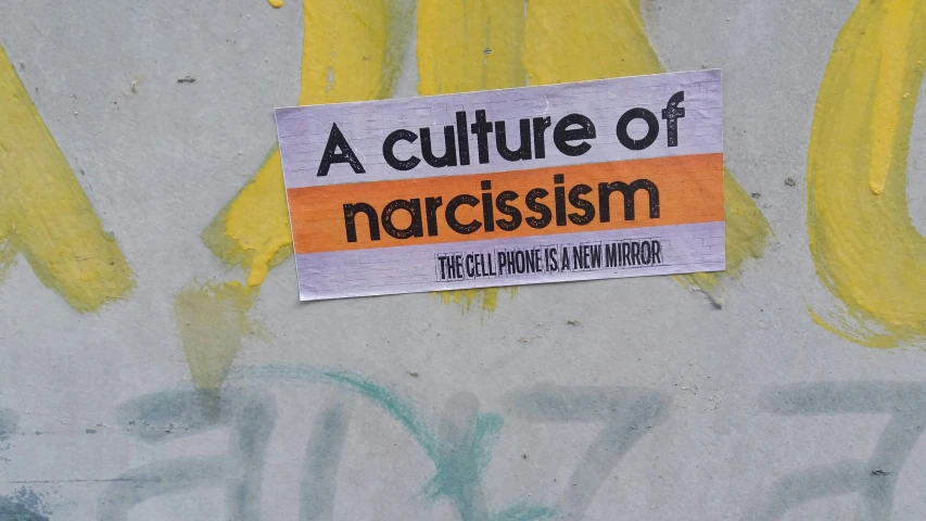 a sign posted on the side of a building, reading a culture of narcissm