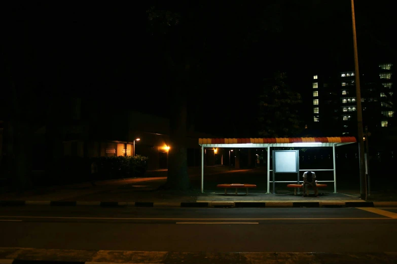 an empty bus stop with two people sitting on a bench at night