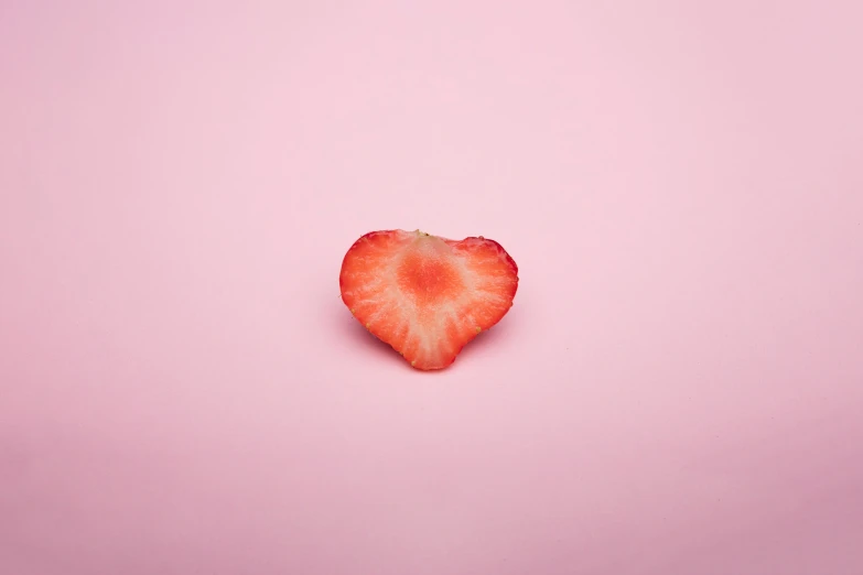 a piece of strawberry in the shape of a heart on a pink surface