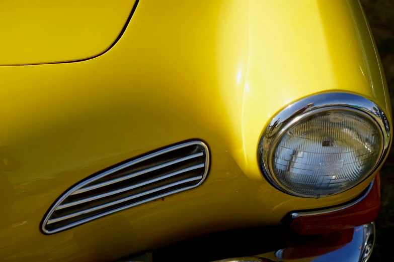 the light reflects off of the yellow front bumper of a vintage vehicle