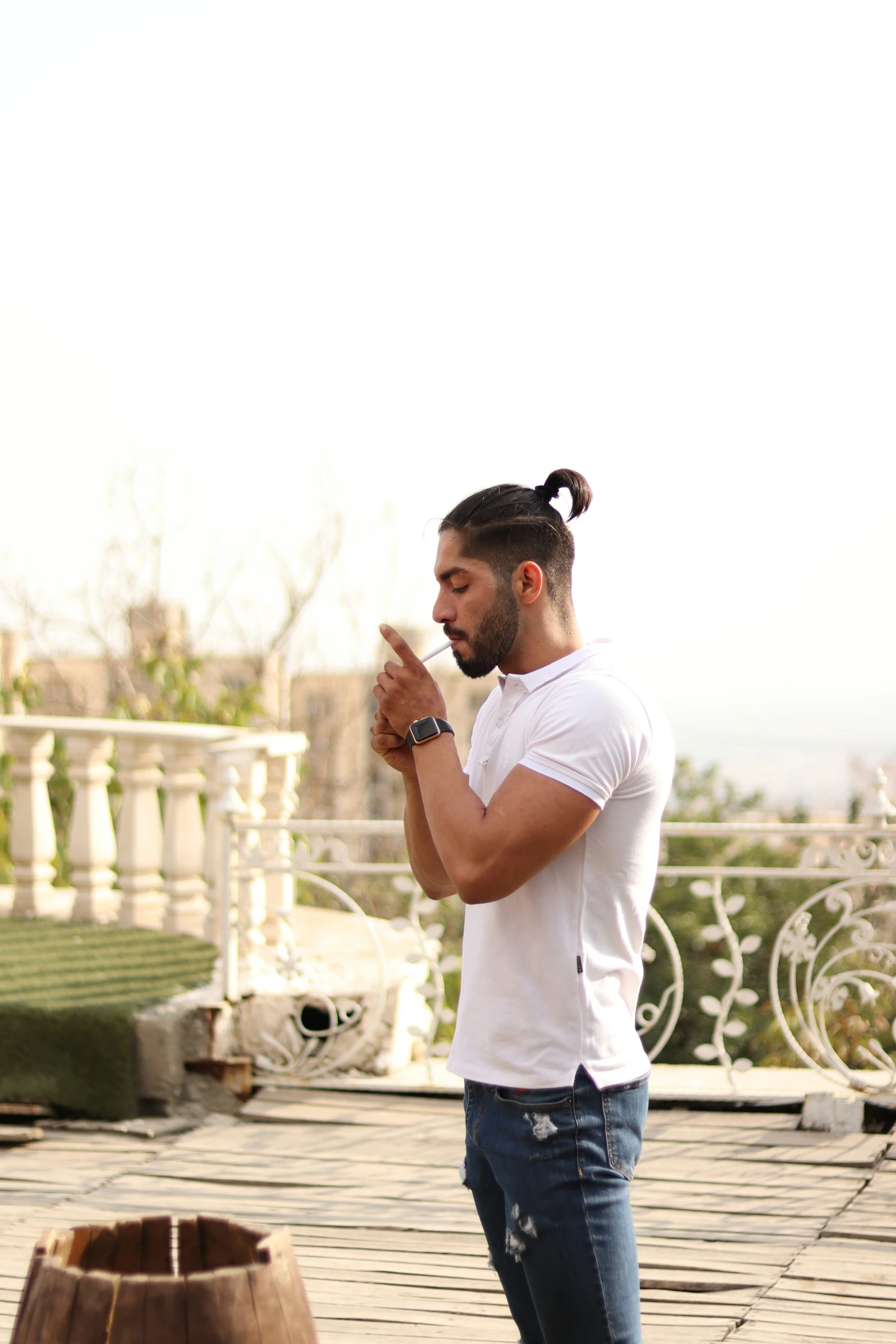 a man with a ponytail in a white shirt stands on a rooftop