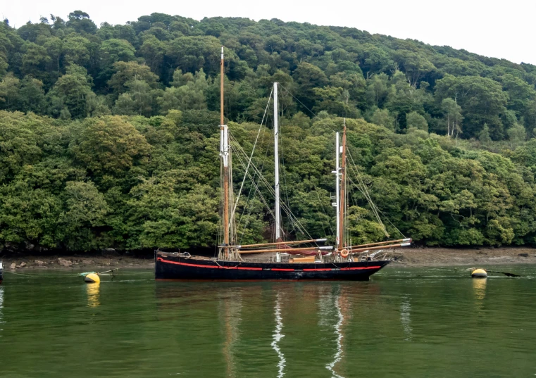 the sail boat is sailing along the river with the hills in the background