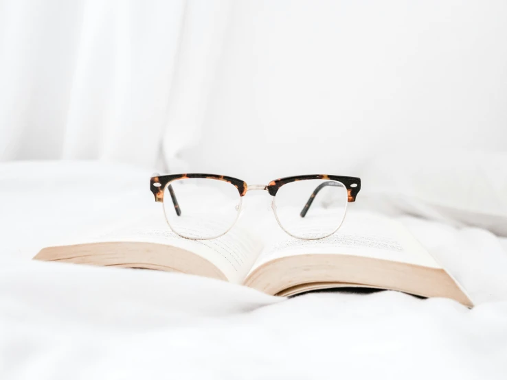 eyeglasses are reading an open book on a white bed