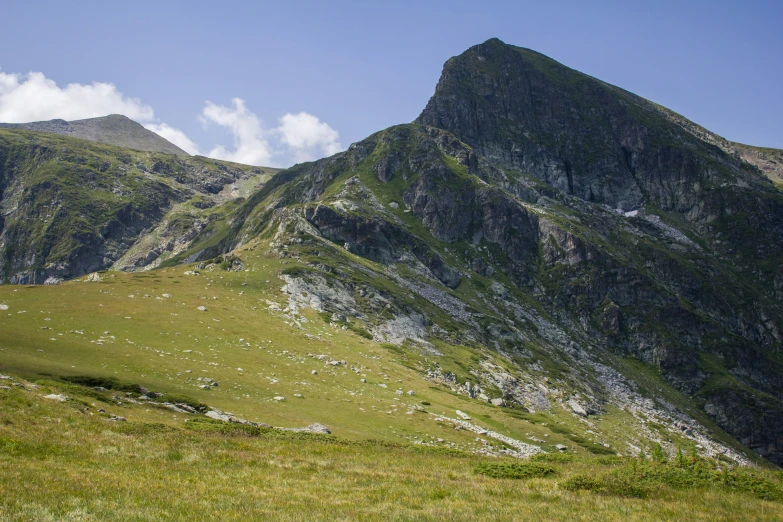 green grass and mountain side with sky in background