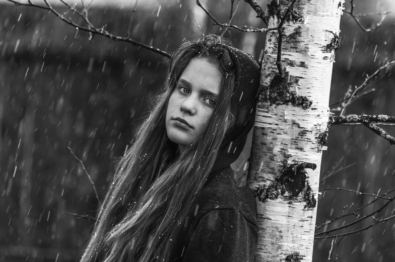 a woman in the woods under a tree with rain falling