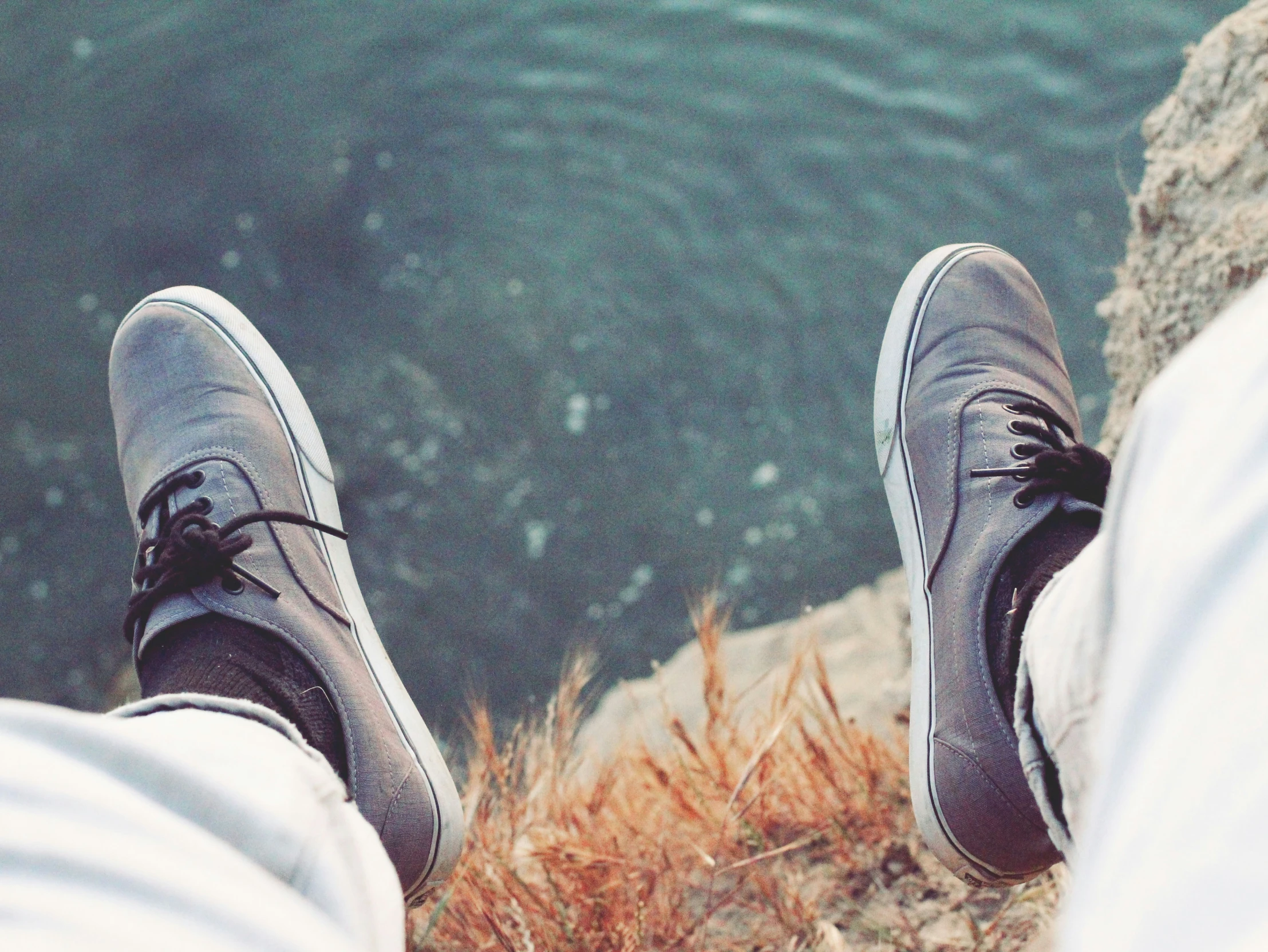 someones feet up on the rocks of a hill overlooking water