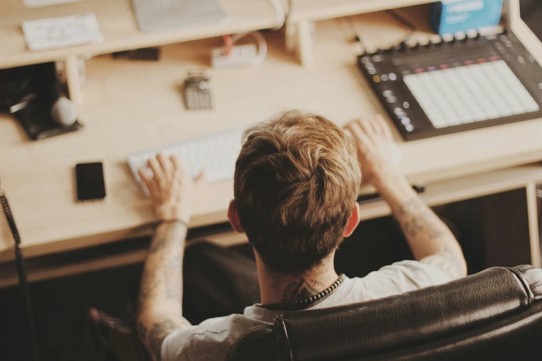 the back view of a man sitting in front of a keyboard and monitors