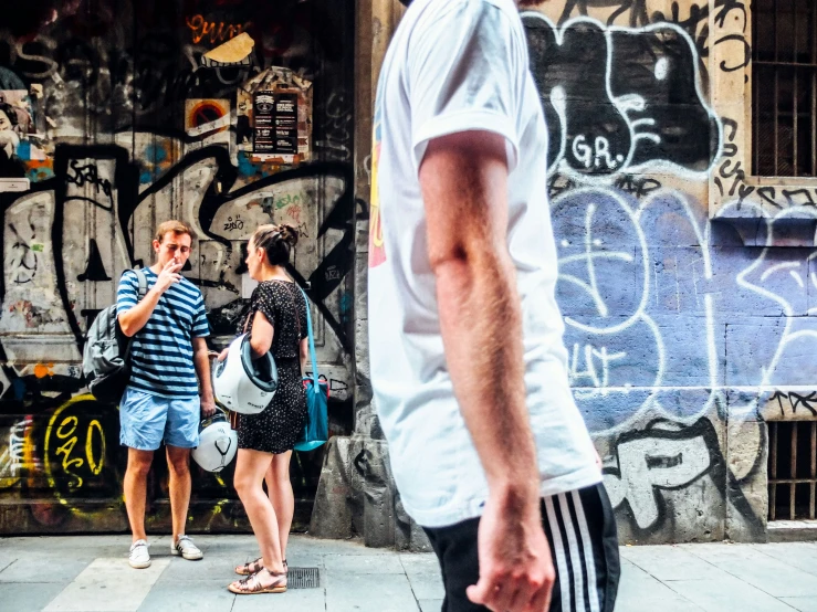 a group of people standing on a sidewalk with graffiti on the wall