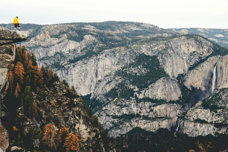 person sitting on top of a rock cliff watching mountains