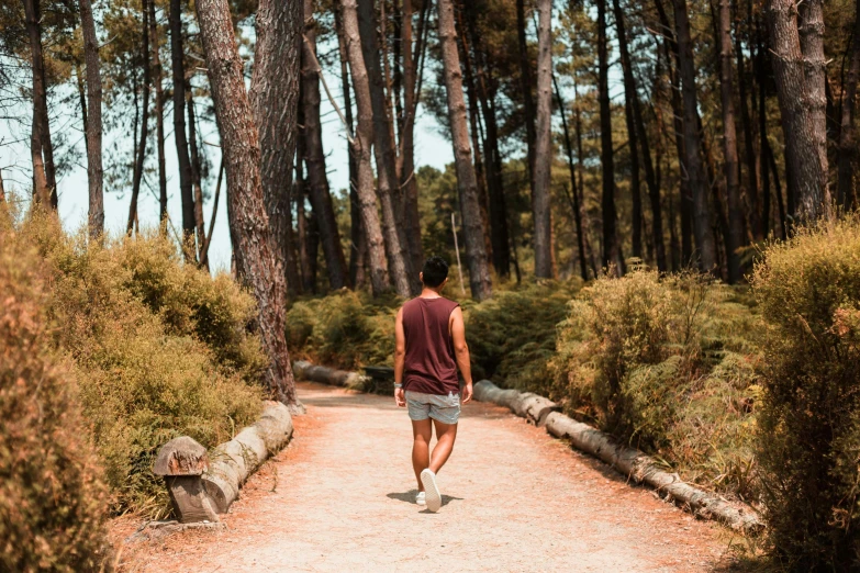 a man in maroon shirt and blue shorts walking on a path near trees