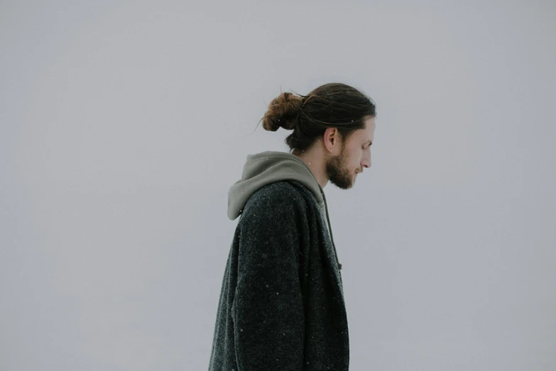 a bearded man in winter attire with a ponytail looks off to his left