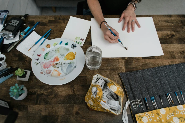 the table has many paintings and paints and a watercolor paper