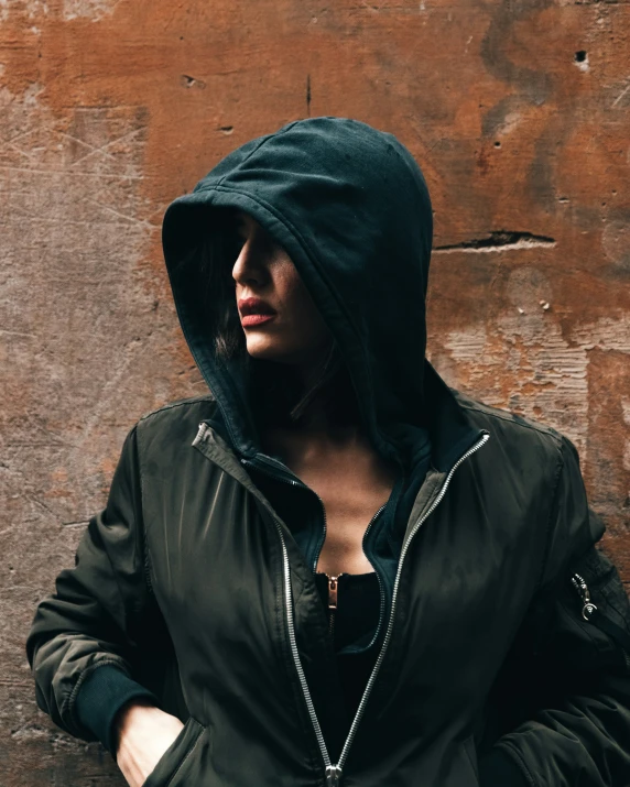 a woman standing near a wall wearing a hoodie