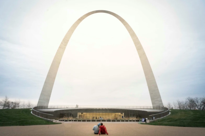 a couple sitting on a bench looking at the view of a large arch