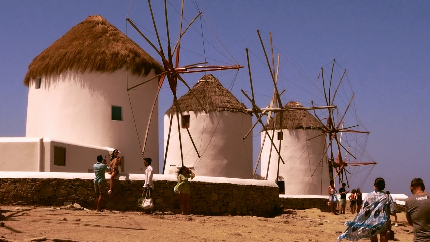 people are walking through the sand by some huts