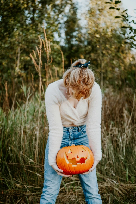 a girl holding a pumpkin wearing denim pants