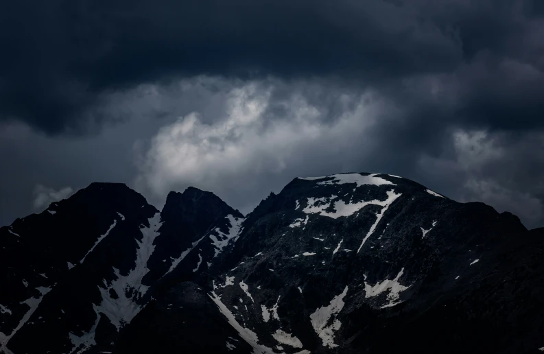 the snow - covered mountains rise above the dark clouds