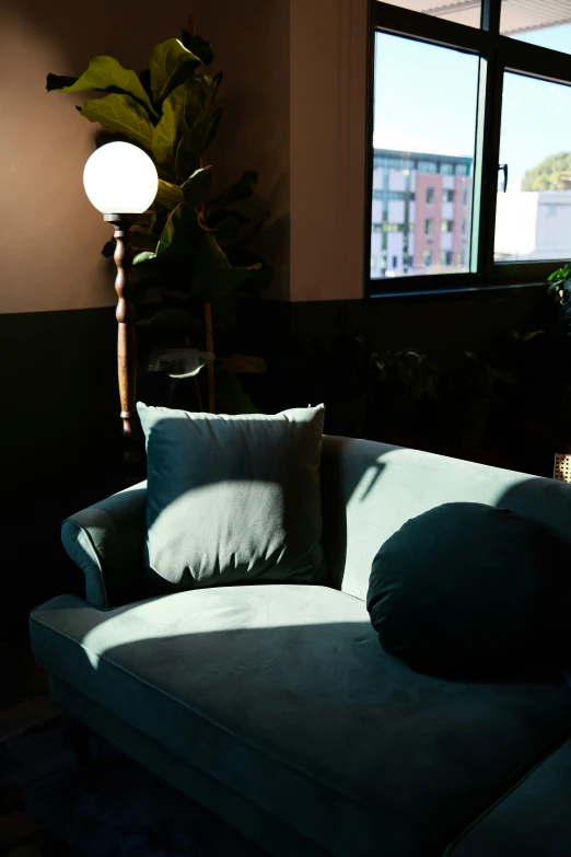 a blue couch with two green pillows next to a window