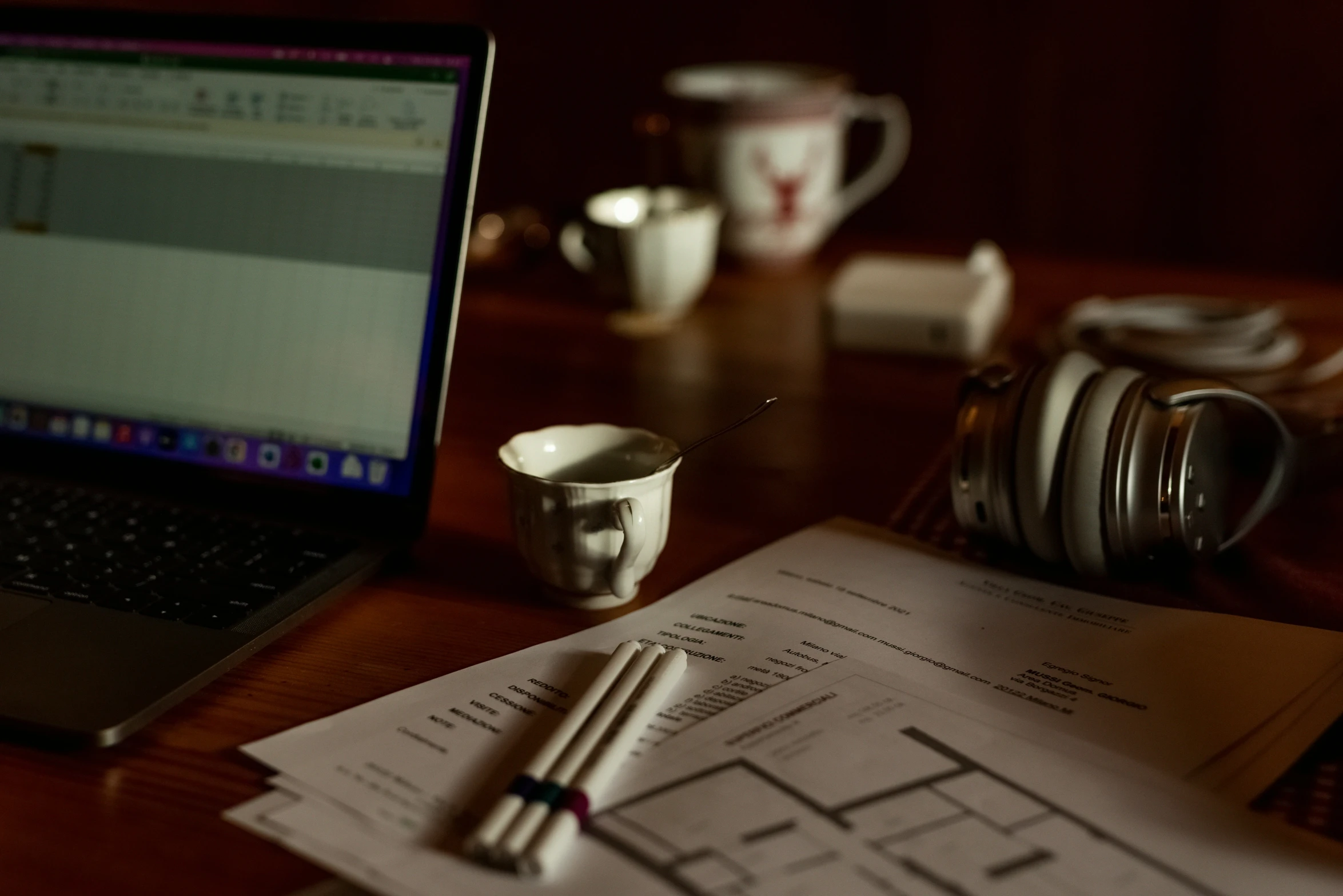 a desk has papers, mugs, and a laptop on it