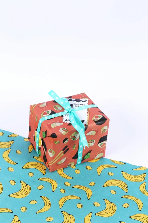 a red and blue present box with ribbon is sitting on an artistic patterned table cloth