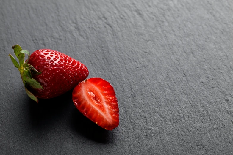 a whole and halved strawberries on a gray table