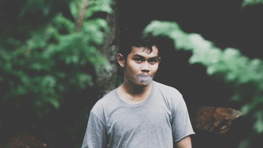 a man in a t - shirt standing in front of a tree