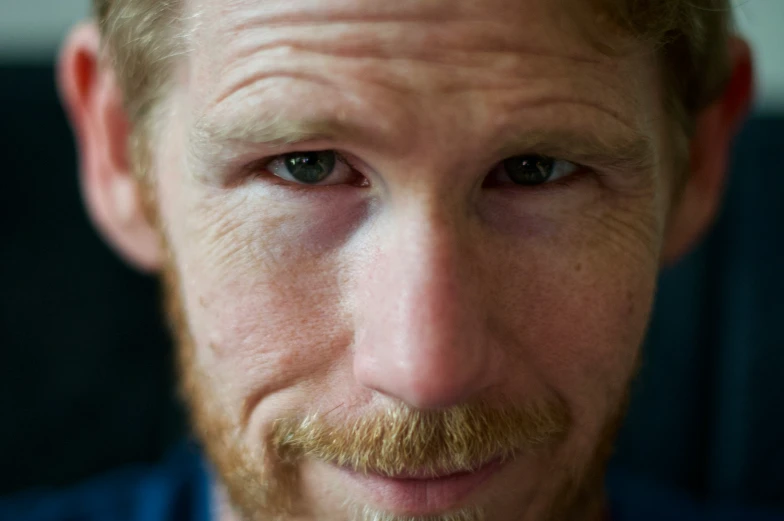 a man with a beard and blue shirt is looking into the camera