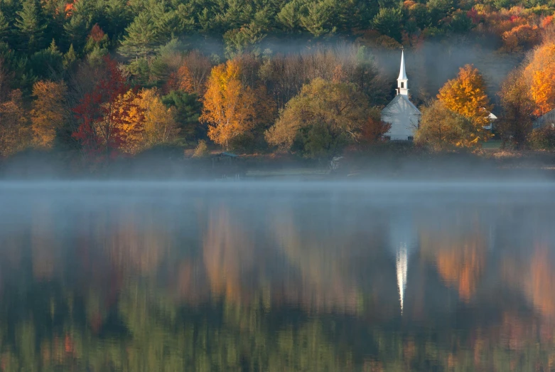 fog hovering over the waters and the spire of an abandoned church in the background