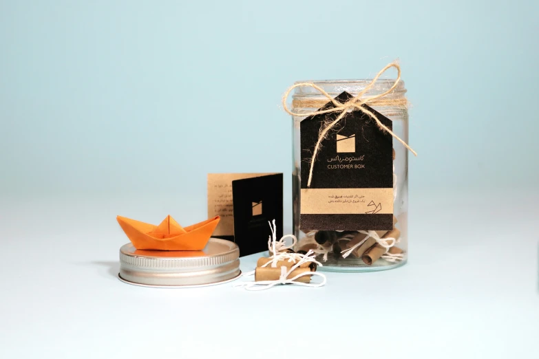 the small orange origami boat is sitting next to a glass jar with its lid open