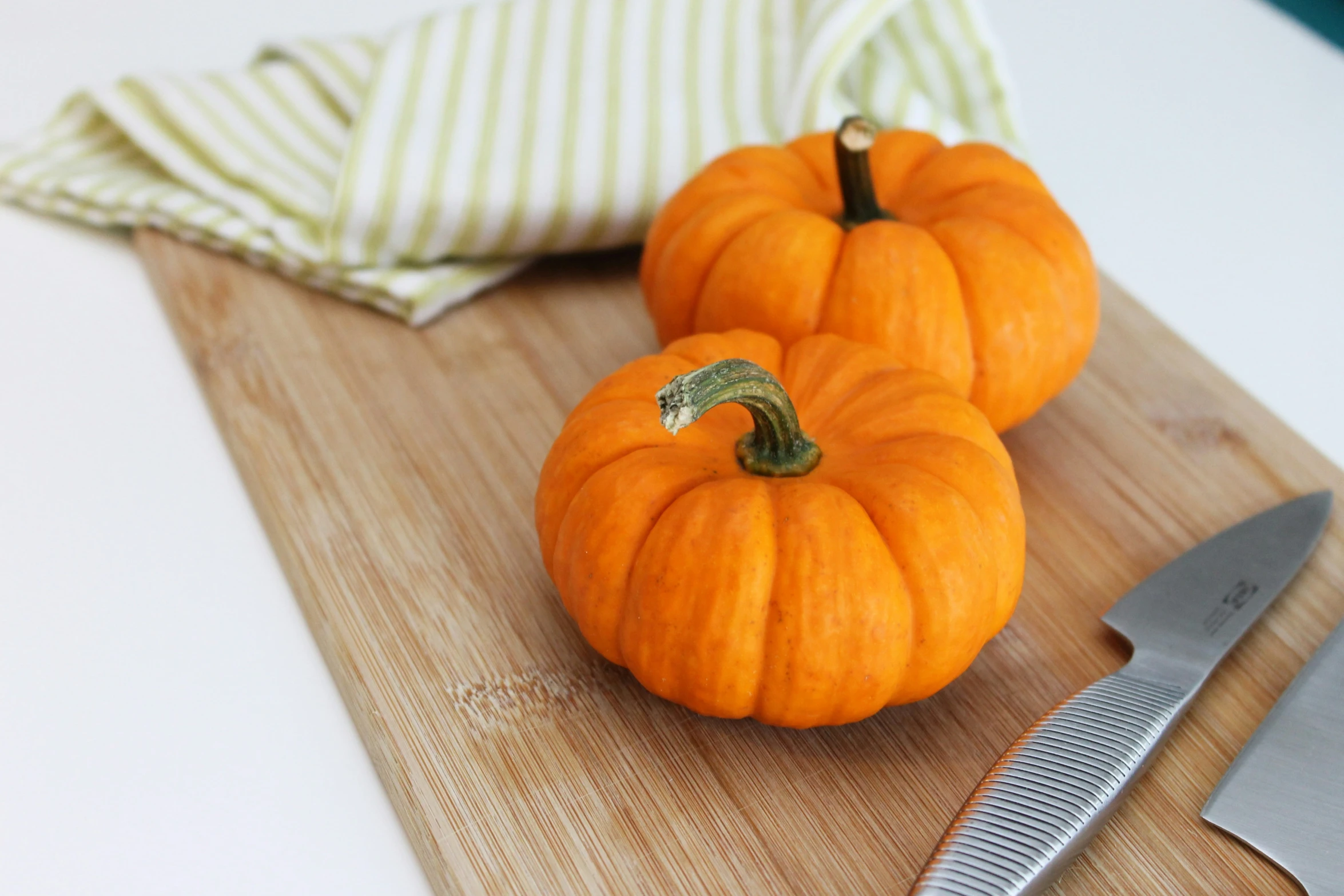 two pumpkins sitting on a  board next to some knives