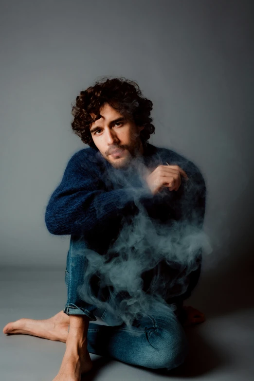 man sitting on the floor smoking while wearing jeans