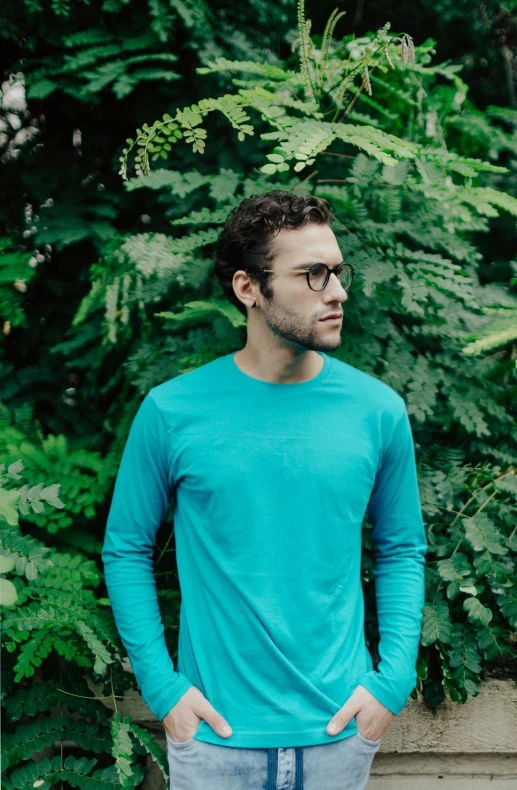 a man in a blue sweater standing in front of a hedge