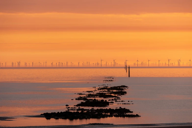 the landscape shows wind turbines, sand and an orange sky