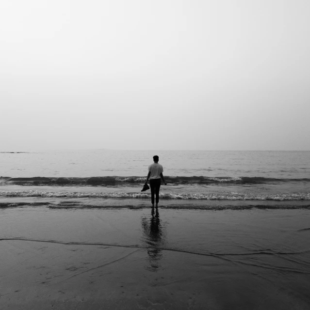 black and white pograph of person walking on the beach
