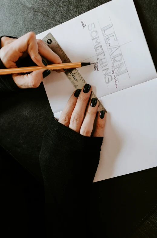 a person's hands hold a pencil and point a piece of paper with an inscription on it