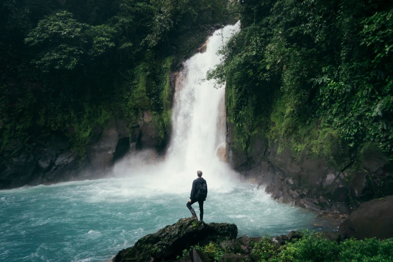 a person standing on a rock in front of a waterfall