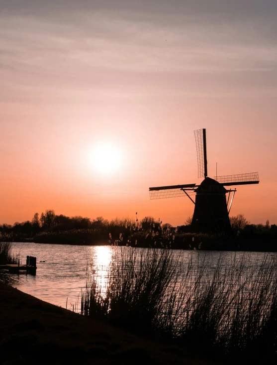 the sun sets over the water behind a windmill