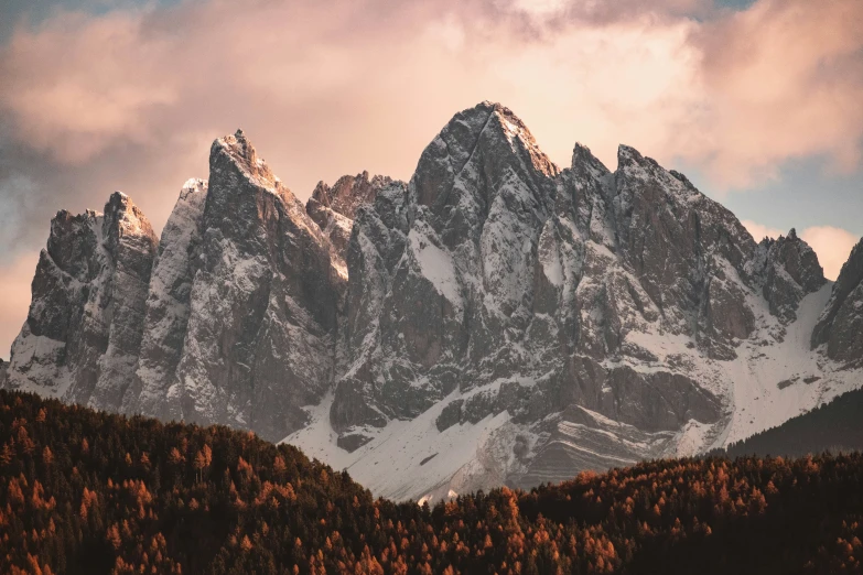 mountains rise above trees and grass under a cloudy sky