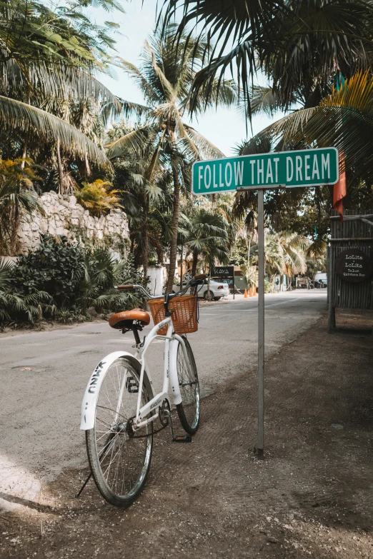 a white bike leaning against a sign on a road