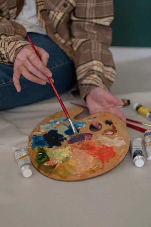 a woman sitting on a table with an easel next to paint and brushes