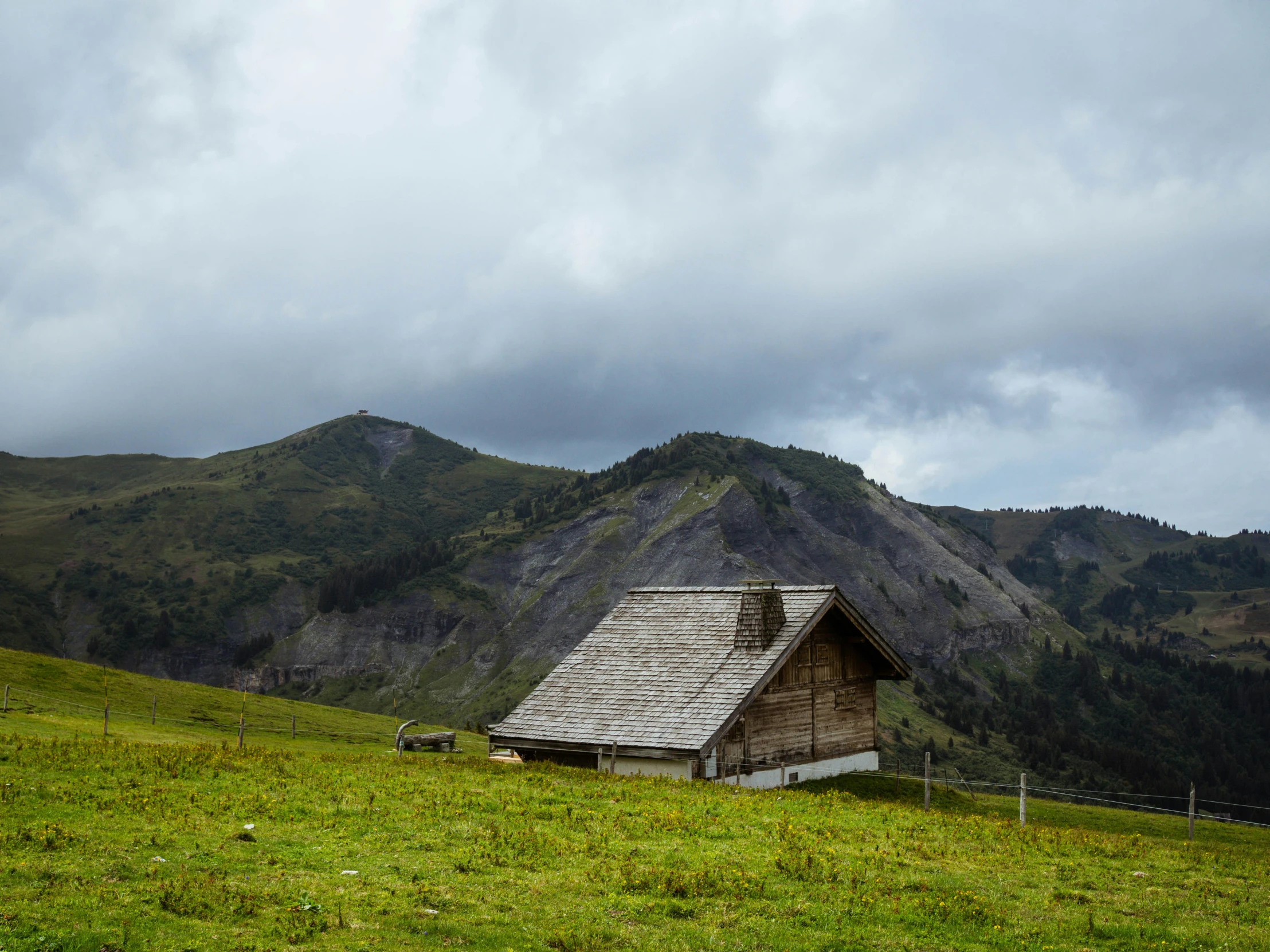 an old log house with a roof in a grassy area near mountains