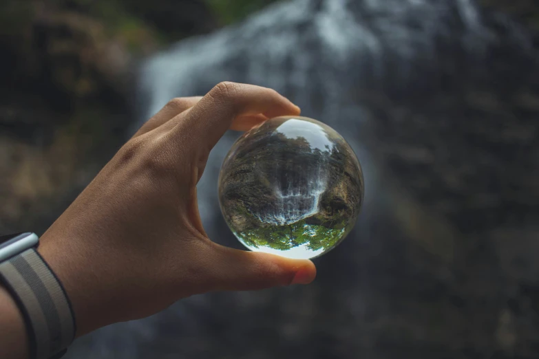 hand holding a glass ball looking at a waterfall